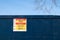 Industrial warning sign stating danger and risk of presecution on a tall blue wall or fence.