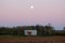 Industrial water pumping station inside concrete structure in middle of local field at sunset with visible full Moon above