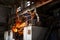 Industrial workers in protective gear operate furnace, handling molten metal at steel mill. Teamwork in heavy industry