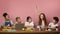 Industrious red haired girl with friends studying at desk against pink background, blank space