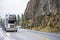 Industry standard big rig semi truck car hauler transporting cars running on the winding mountain road with rock wall on the side