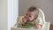 An infant 7-month caucasian girl is eating with bare hands.