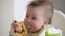 An infant 7-month caucasian girl is eating broccoli with bare hands.