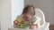 An infant 7-month caucasian girl is eating pasta with bare hands.