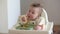 An infant 7-month caucasian girl is eating pasta with bare hands