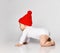 Infant baby blond boy toddler in white bodysuit and red hat is interested in something going to crawl out on all fours