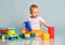 Infant baby boy toddler in yellow pants and white t-shirt is sitting on the floor surrounded by colorful toys, playing