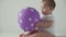 Infant, childhood concept - happy funny playfull toddler kid 8 month baby girl play with purple ballon on birthday party