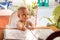 Infant girl is sitting on a baby`s high chair in a street cafe. Children reading chooses and studies the menu in the restaurant