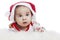 The Infant lies on his stomach in a Santa Claus hat with a surprised, funny face. New Year and Christmas celebration. Close-up.