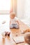 Infant little cooker boy helps to make cakes sitting at table with flour spread.