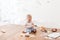 Infant little cooker boy helps to make cakes sitting at table with flour spread.