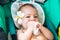 Infant pulls a napkin in his mouth. Little baby at 8 months old with a frangipani flower behind the ear. Sits in a travel stroller