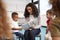 Infant school boy pointing in a book held by the female teacher, sitting with kids in a circle on chairs in the classroom, close u