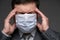 Infected man has a headache and symptoms of the disease, he touches his forehead with his hand, has a protective face mask -