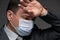 Infected man has a headache and symptoms of the disease, he touches his forehead with his hand, has a protective face mask -