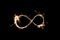 Infinity sign made with sparkler starlight dark black background bright warm isolated