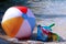 Inflatable beach ball, bucket, shovel and diving goggles on the beach in Italy with sea in the background - summer holiday