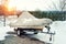 Inflatable luxury fishing motorboat wrapped in cover standing over trailer for winter period seasonal storage at