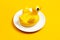 Inflatable mini yellow chicken or duckling on white plate on yellow background. Creative food concept tobacco chicken. Flat lay