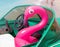 Inflatable pink flamingo sitting inside the green powerboat on the white seat with legs running on the sand beach on the