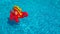 An inflatable red dinosaur in clear rippling pool water. Funny baby toy floats isolated in blue water. Summer vacation