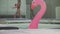 Inflatable rubber pink flamingo floating in a pool on the background of a passing beautiful girl in a bathing suit with
