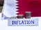 Inflation in Qatar concept. Handwritten Inflation on a paper board, growing up arrow, coins and flag of Qatar in the background