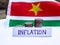 Inflation in Suriname concept. Handwritten Inflation on a paper board, growing up arrow, coins and flag of Suriname in the
