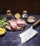 Ingredients for cooking 2 raw chicken meat cleaver steak seasoning and lemon herbs dark blue wooden background close up