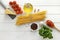 Ingredients for cooking bucatini with tomatoes, basil, cheese and garlic on white wooden background.