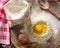 Ingredients for cooking dough or bread. Broken egg on top of a bunch of white rye flour. Dark wooden background.