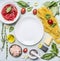 Ingredients for cooking pasta, tomatoes in own juice, basil, shrimp, grater, cherry tomatoes, laid around a white plate place