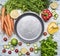 Ingredients for cooking salad cherry tomatoes, lettuce, peppers, spices and oil laid out around vintage frying pan on wooden rus