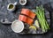 Ingredients for lunch - fresh raw organic salmon, green asparagus and rice on a dark background, top view