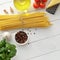 Ingredients for mediterranean pasta dish: bucatini or spaghetti, tomatoes, basil, spice on white wooden background.