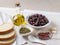 Ingredients for tapenade: cured or dried olives in a white bowl, anchovy fillet, capers, garlic, olive oil and bread on a white