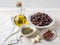 Ingredients for tapenade: cured or dried olives in a white bowl, anchovy fillet, capers, garlic and olive oil on a white rustic