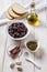 Ingredients for tapenade: dried or cured olives in a white bowl, anchovy fillet, capers, garlic, olive oil and bread on a white