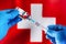Injecting dose of vaccine in syringe for infections prevention in front of the Swiss flag