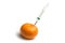injecting with a syringe into a tangerine on white background