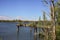 Inlet with wooden poles and a barge by the shore in a forest next to an industrial complex on a sunny day