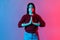 Inner peace, concentrated mind. Neon light portrait of calm beautiful woman holding hands up in namaste gesture