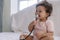 Innocence toddler girl sitting on the white bed while holding stethoscope in her hand at home. Mixed race little doctor baby