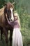 Innocent blonde girl with horse in forest. beautiful Caucasian girl with long blonde hair in a pink dress hugs a brown horse.