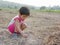 Innocent little Asian baby girl trying to plant dry grasses on the ground to keep them alive