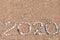 The inscription `2020` laid out by sea pebbles on the sand of the beach. Summer lettering on the coast with copy space for text