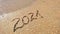 The inscription 2021 on the sand is erased by the sea wave. Happy new year 2022 concept.