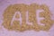 The inscription of ale with malt grains on a lilac textile background. Craft beer brewing from grain barley malt in process. Ale