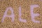 The inscription of ale with malt grains on a lilac textile background. Craft beer brewing from grain barley malt in process. Ale